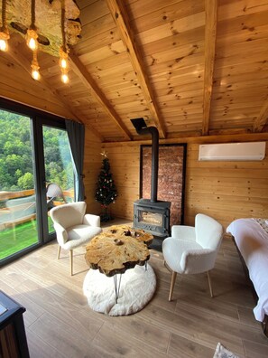 L’intérieur chaleureux d’un chalet avec un plafond en bois, une cheminée, un sapin de Noël et une grande fenêtre donnant sur le paysage extérieur.