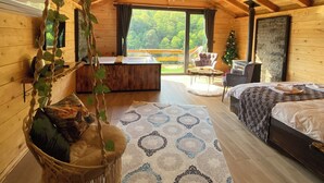 A cozy log cabin bedroom with a hanging chair, a bed, a small table, and a view of the outdoors.