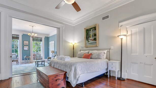 Quarto com cama, mesas de cabeceira, penteadeira, armário e um ventilador de teto, além de um quadro na parede.