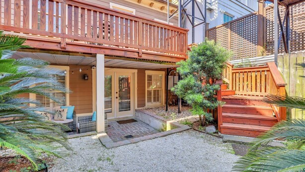 A covered outdoor area with a wooden deck, a small seating area with cushions, and a potted plant.