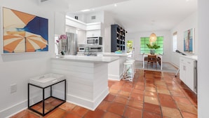 A modern kitchen with white cabinetry, a central island, and a dining area with a table and chairs. - BANYAN ROSE ~ Renovated 4 Bedroom, 2 Bathroom Midtown Home w/ Pool! (Key West)