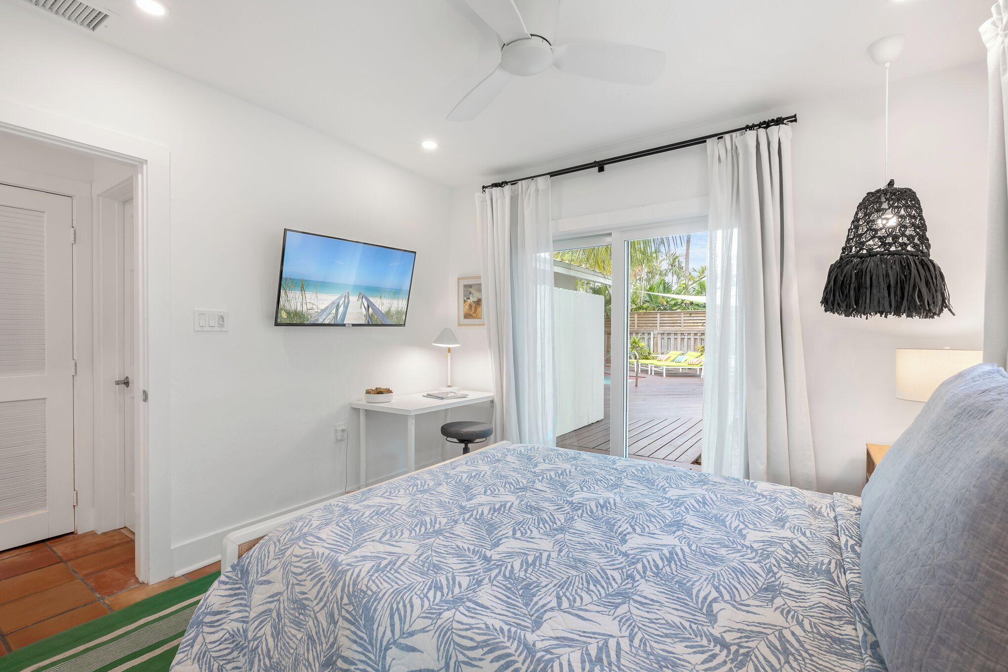 Un dormitorio con cama, escritorio, silla, televisión y vistas al exterior.