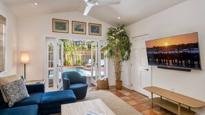 A living room with a blue sofa, a wooden bench, a large potted plant, and a TV on the wall. - BANYAN ROSE ~ Renovated 4 Bedroom, 2 Bathroom Midtown Home w/ Pool! (Key West)