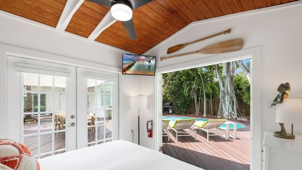 A bedroom with a large bed, a ceiling fan, a TV, and a view of a pool and outdoor furniture. - BANYAN ROSE ~ Renovated 4 Bedroom, 2 Bathroom Midtown Home w/ Pool! (Key West)