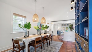 A modern kitchen with a dining area, featuring a white countertop, wooden chairs, and hanging pendant lights. - BANYAN ROSE ~ Renovated 4 Bedroom, 2 Bathroom Midtown Home w/ Pool! (Key West)