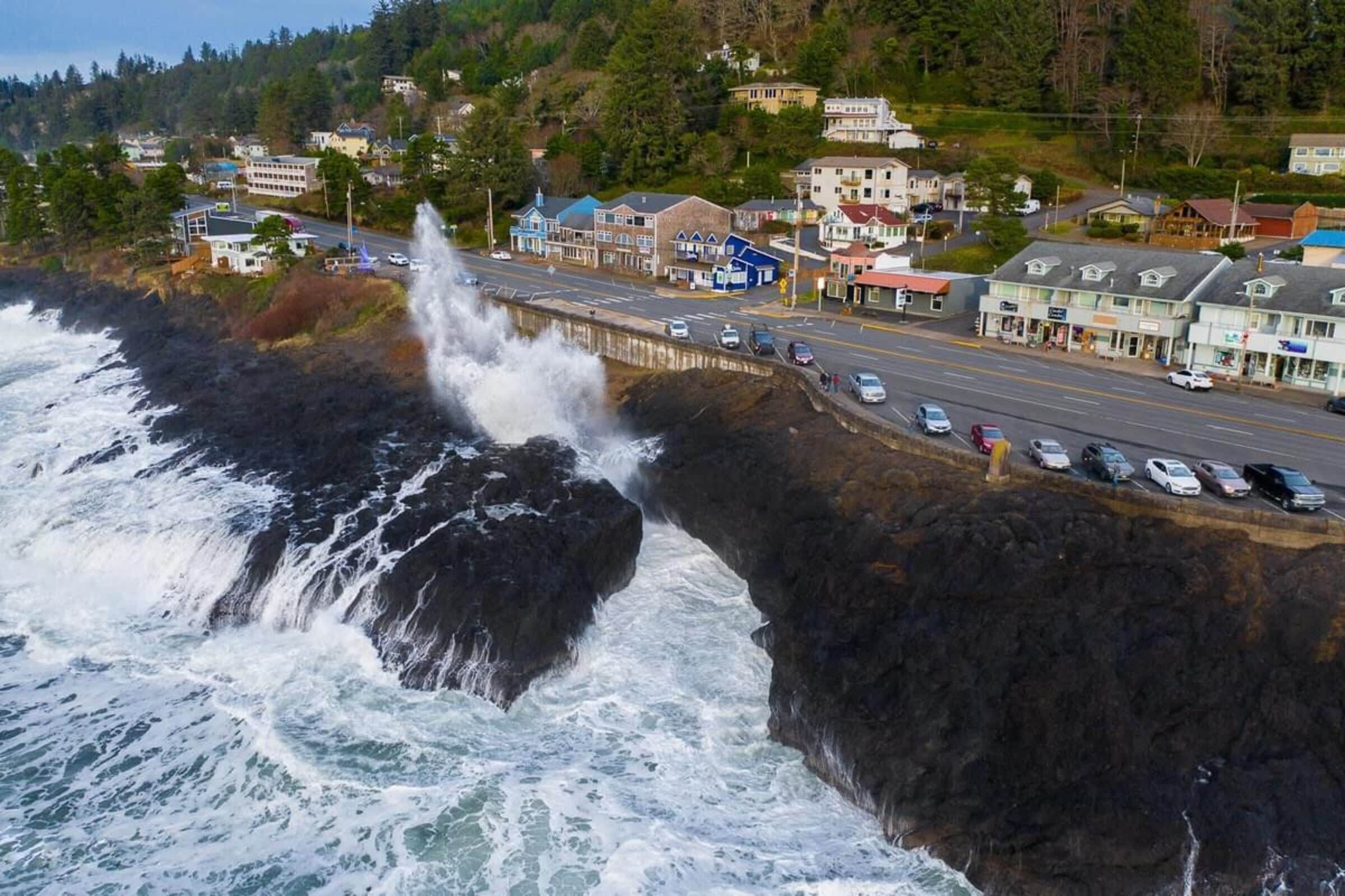 A coastal town with a rocky shoreline, a road with parked cars, and buildings with various architectural styles.