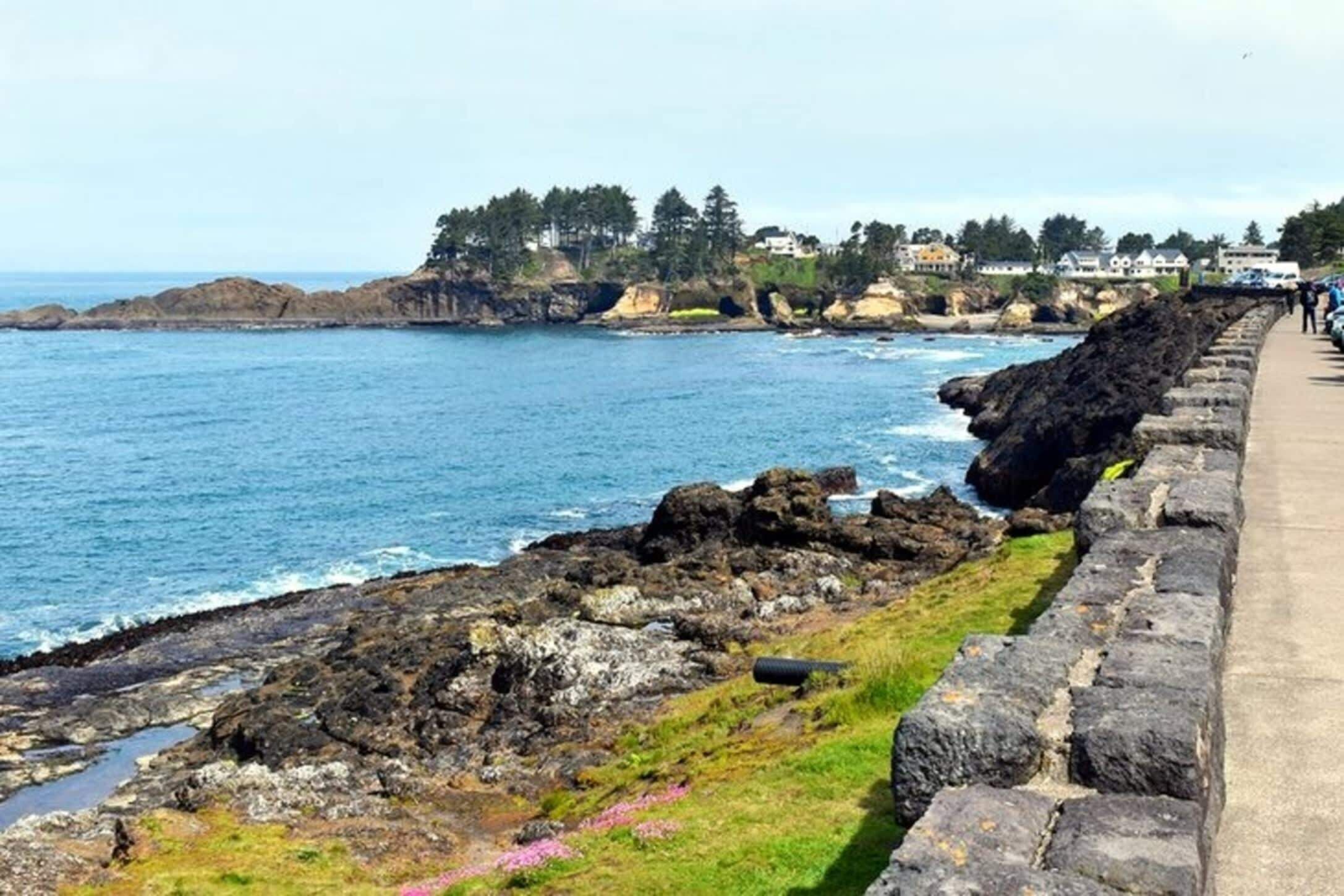 Une promenade en bord de mer, avec une côte rocheuse, un mur de pierres et une vue sur la mer et les bâtiments situés au loin.