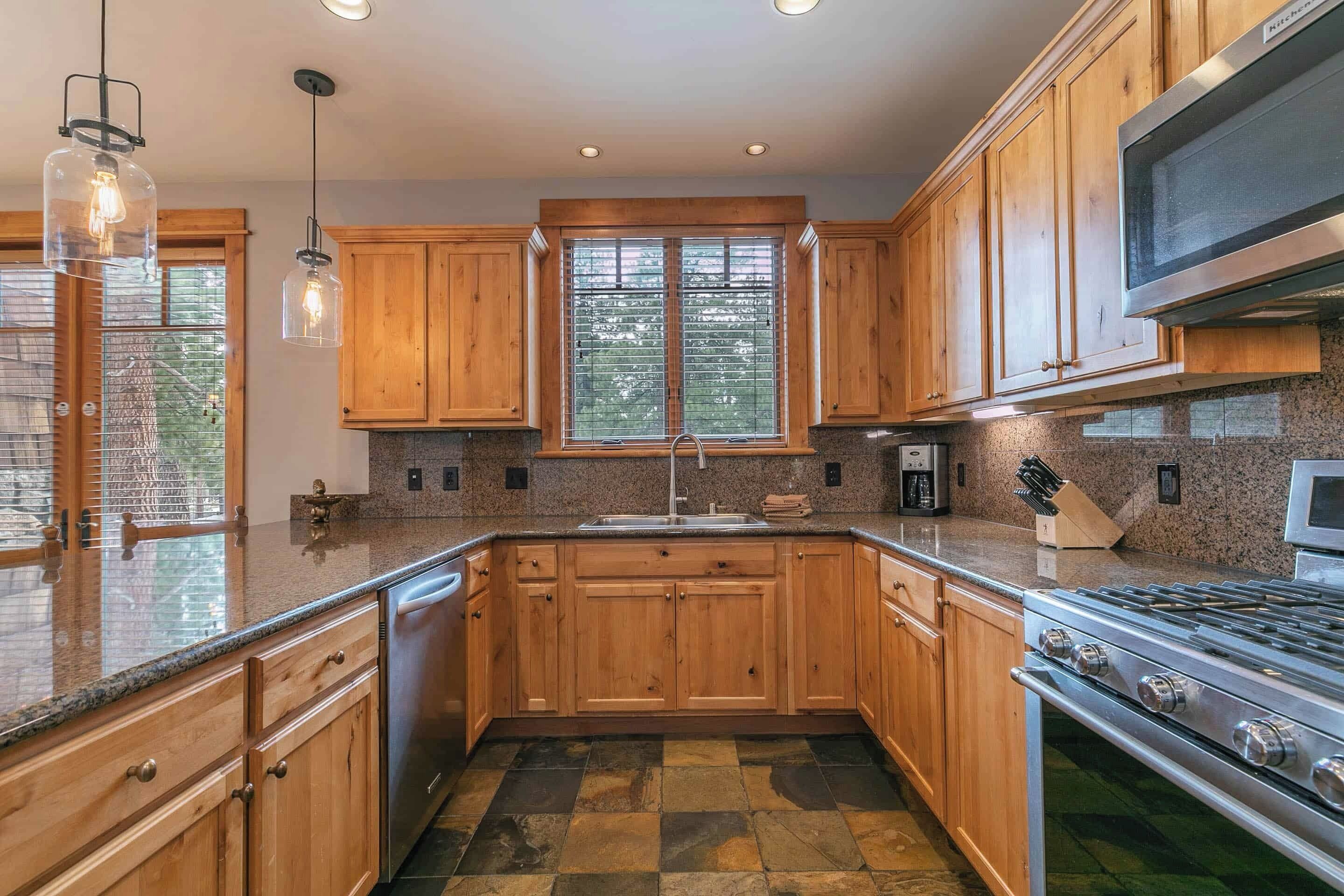 Una cocina con armarios de madera, encimera de granito, estufa de acero inoxidable e iluminación colgante.