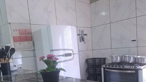 A kitchen with a marble countertop, a white refrigerator, a stove, and a potted plant. - Chacara Rancho da Cris (Ibiuna)