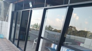 A building with large glass windows and a tiled patio area. - Chacara Rancho da Cris (Ibiuna)