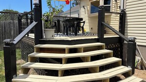 A wooden staircase leading to a deck with outdoor furniture, a potted plant, and a house in the background. - Great for families or corporate travelers. (Omaha)