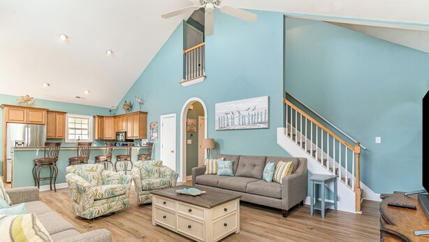 A spacious living area with a high ceiling, wooden flooring, a staircase, and a kitchen in the background. - 242 Georges Bay Road (Whole) located in Bermuda Bay. (Murrells Inlet)