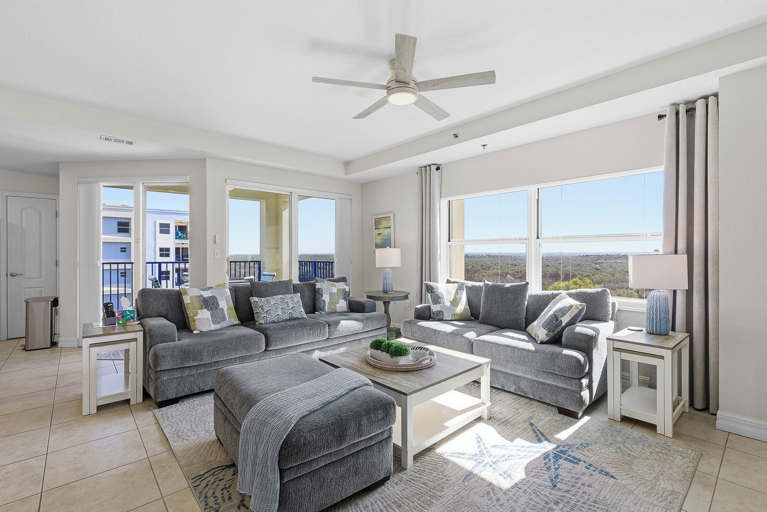 A spacious living room with grey sofas, a coffee table, and a ceiling fan.