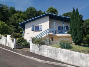Ein zweistöckiges Haus mit blauem Dach, einem Balkon und einer Steinmauer davor.