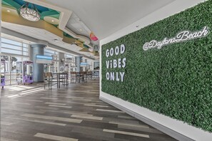 A spacious indoor area with a green wall displaying the text 'GOOD VIBES ONLY' and a sign '@DaytonaBeach'.