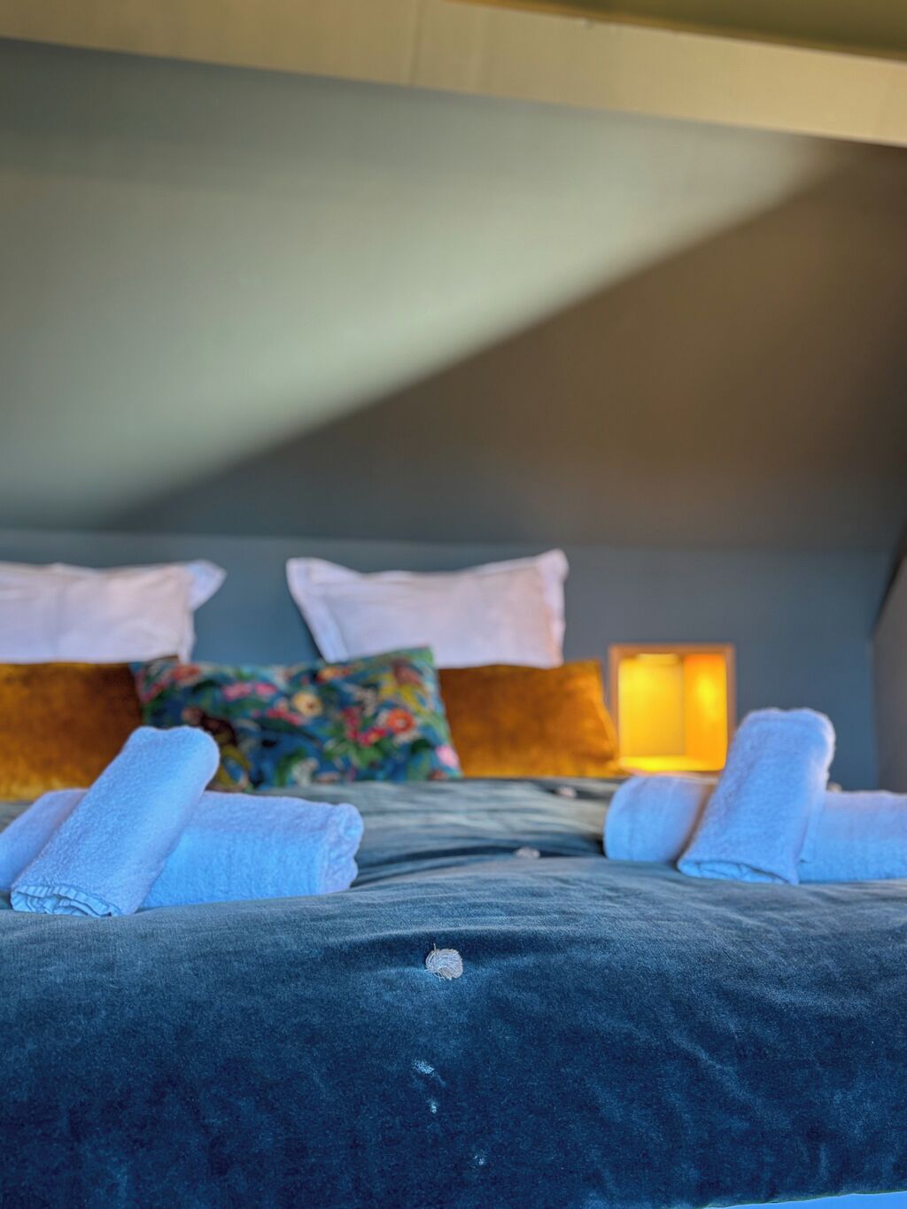A hotel room with a bed, pillows, and a nightstand with a lamp.