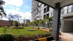 A modern building with a covered outdoor area featuring a well-maintained garden with various plants and flowers. - Alina Ridge (Nairobi)