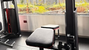 A gym with exercise equipment, a bench, and a view of a garden through a window. - Alina Ridge (Nairobi)