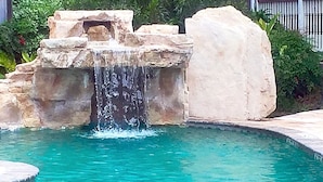 Piscina con una cascada, rodeada de estructuras de piedra y vegetación.