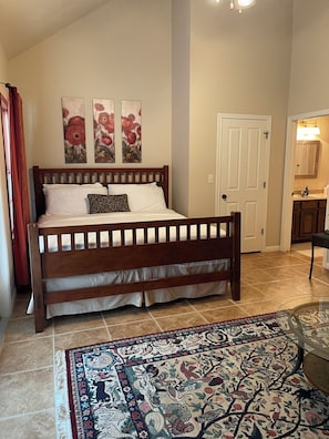 Une chambre à coucher avec un lit en bois, un tapis à motifs, une porte et une petite salle de bain visible à travers une porte ouverte.
