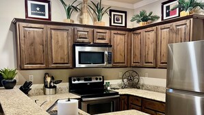 Una cocina con armarios de madera, un refrigerador de acero inoxidable, un microondas y encimeras de granito.