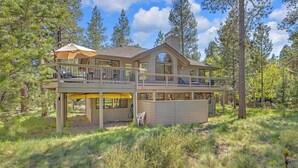 A two-story house with a balcony and a covered patio area, surrounded by trees. - Pet Friendly, AC, Hot tub, Ping pong, guest fav (Sunriver)