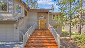 A two-story house with a wooden staircase leading to a front door, surrounded by trees and a clear sky. - Pet Friendly, AC, Hot tub, Ping pong, guest fav (Sunriver)