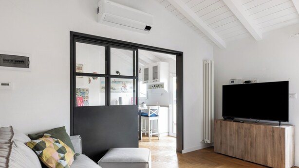 Uma sala de estar moderna com um sofá, uma televisão sobre um móvel de madeira e uma janela grande.