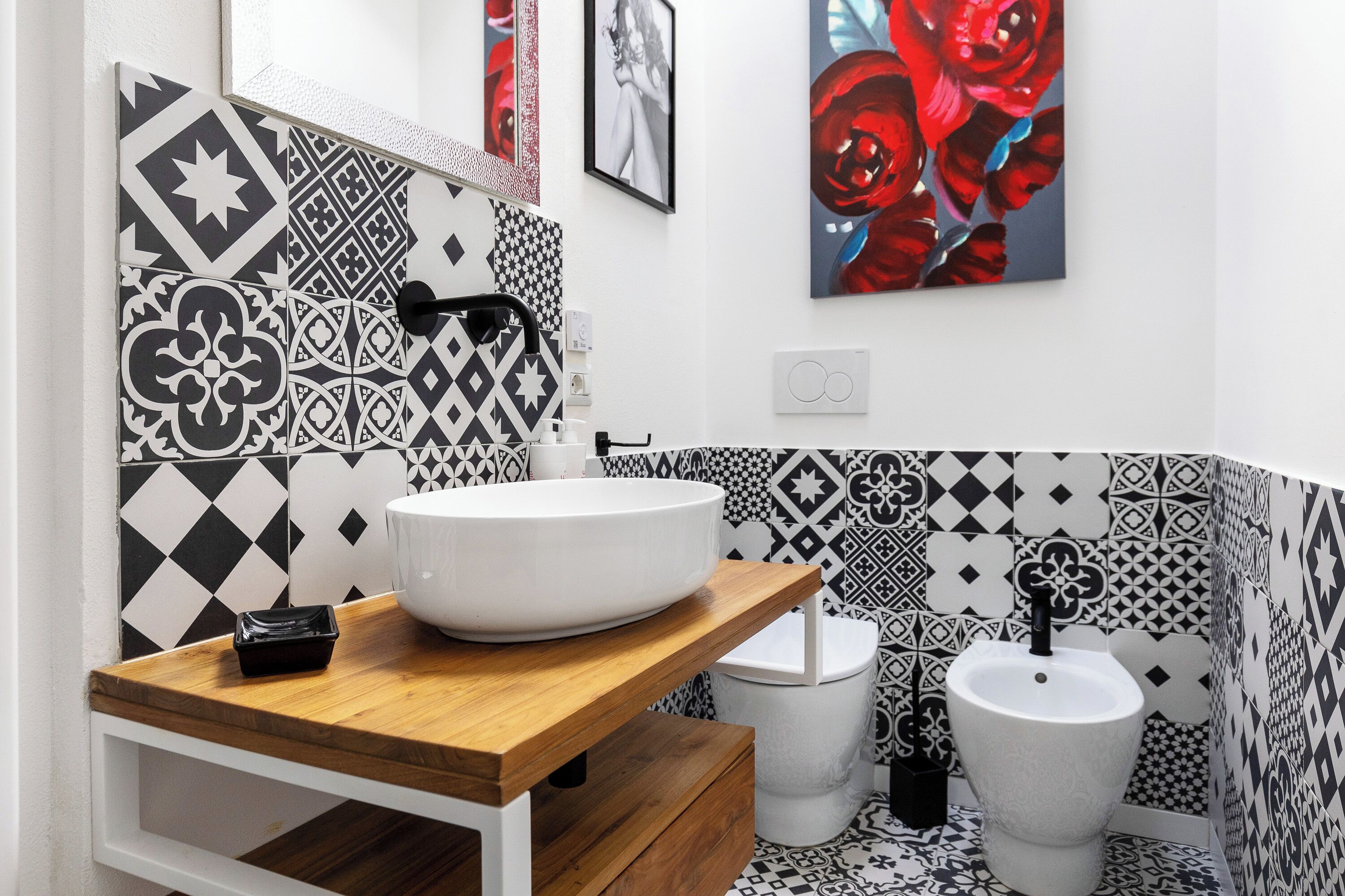 A bathroom with a white sink, black and white patterned tiles, a wooden countertop, and a white toilet.