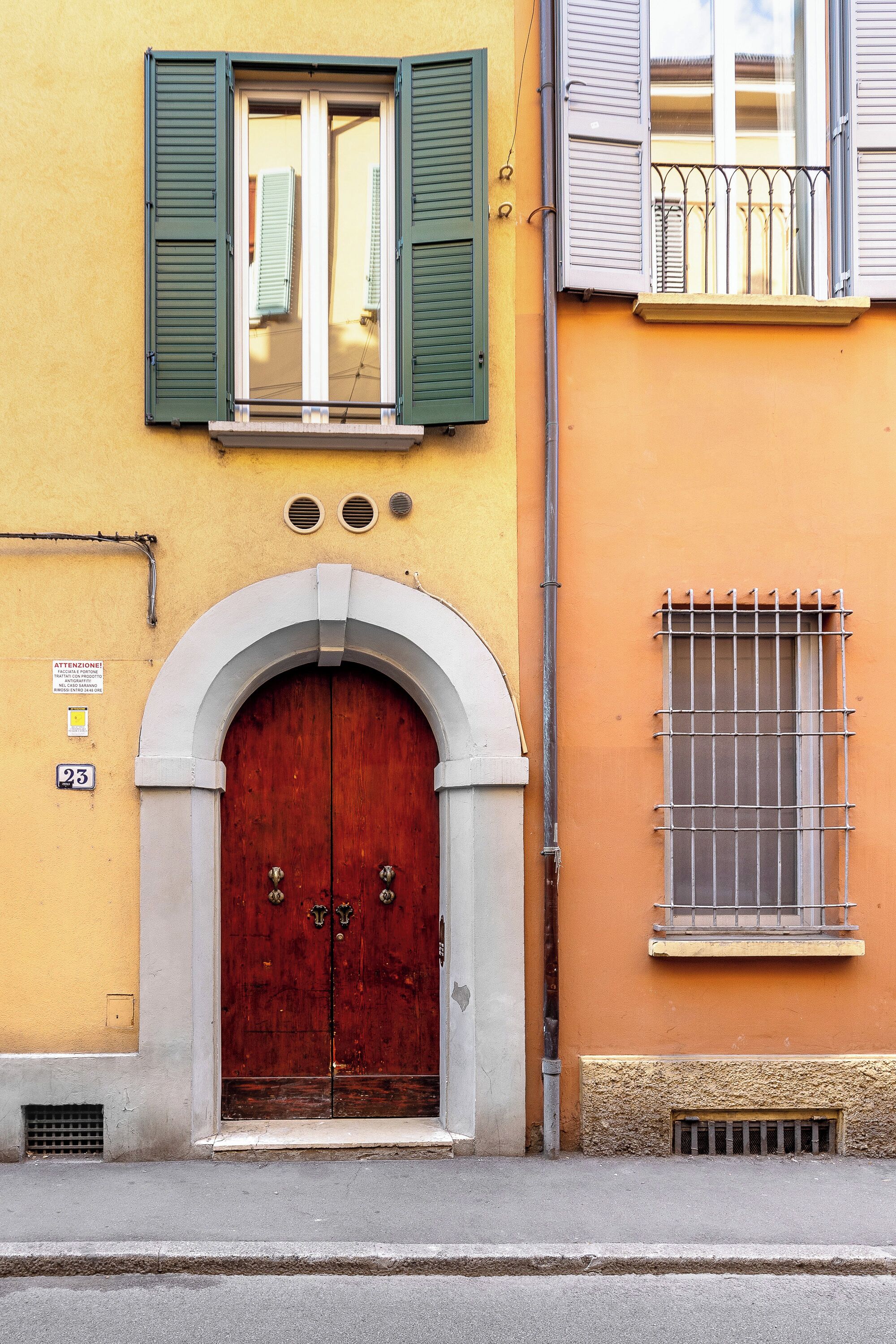 A building with a large wooden double door, green shutters, and a small window with a metal grille.