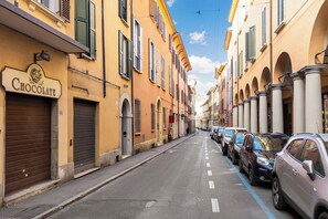 A street lined with parked cars and buildings with shuttered shops. - Appartamento Guerrazzi by Wonderful Italy (Bologna)
