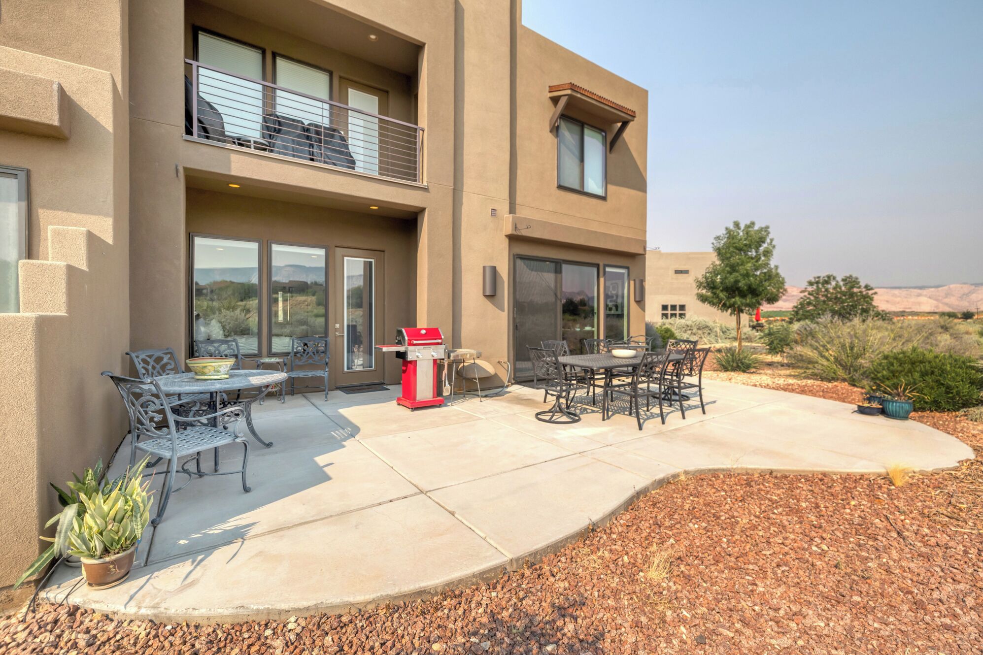 Un bâtiment à deux étages doté d’un patio aménagé avec du mobilier d’extérieur, un barbecue et une vue sur le paysage environnant.