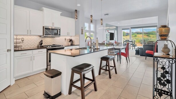 A modern kitchen with white cabinets, a central island, and a dining area with red chairs. - Luxe 4BR w/ Canyon Views - 3 King Beds & Hot Tub (St. George)