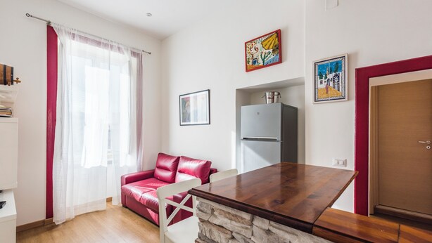 Ein kompakter Wohnraum mit Küchenzeile, einem roten Sofa, einem Esstisch und einer Wand mit Steinverkleidung.