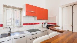 Eine kleine Küche mit weißen Schränken, einer roten Spritzschutzwand, einem eingebauten Backofen und einem Holzespeisetisch.