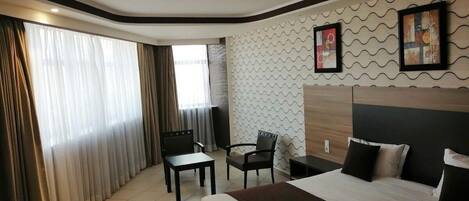 A hotel room with a large bed, two chairs, a small table, and a window with curtains.