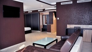 A modern hotel room with a sofa, a glass coffee table, a bed, a TV, and a kitchenette. - Atlantis Akbou (Akbou)