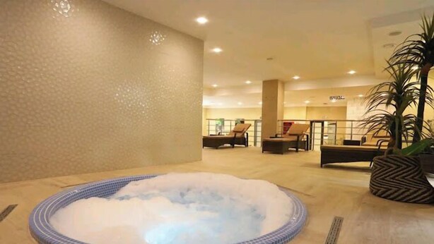 A hot tub in a hotel lobby with tiled flooring, a palm tree, and a seating area in the background. - Atlantis Akbou (Akbou)