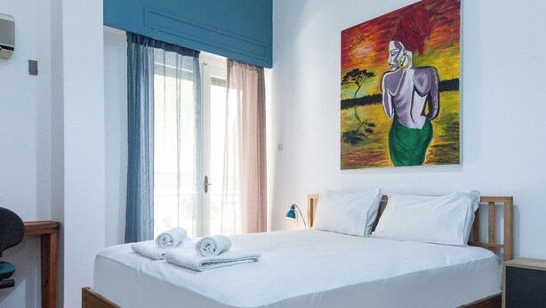 A hotel room with a bed, a painting on the wall, and a window with curtains. - Spacious 2 Bd Pireas Apt w Cozy Balcony (Piraeus)