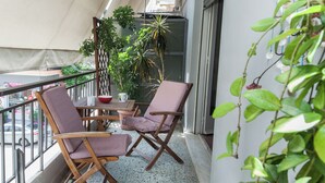 A balcony with two wooden chairs and a small table, surrounded by potted plants. - Spacious 2 Bd Pireas Apt w Cozy Balcony (Piraeus)