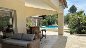Un patio couvert avec un canapé en osier, une petite table et une piscine en arrière-plan.