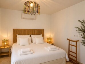 A bedroom with a wooden headboard, white bedding, a decorative hanging light fixture, bedside lamps, and a ladder against the wall. - Les Olicias – Provençal Villa with Private Pool and Panoramic Views (Flayosc)
