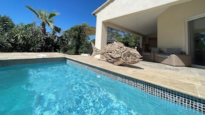 Une piscine à l’eau d’un bleu cristallin, une grande sculpture en bois et un espace de détente extérieur abrité, avec un canapé en osier.