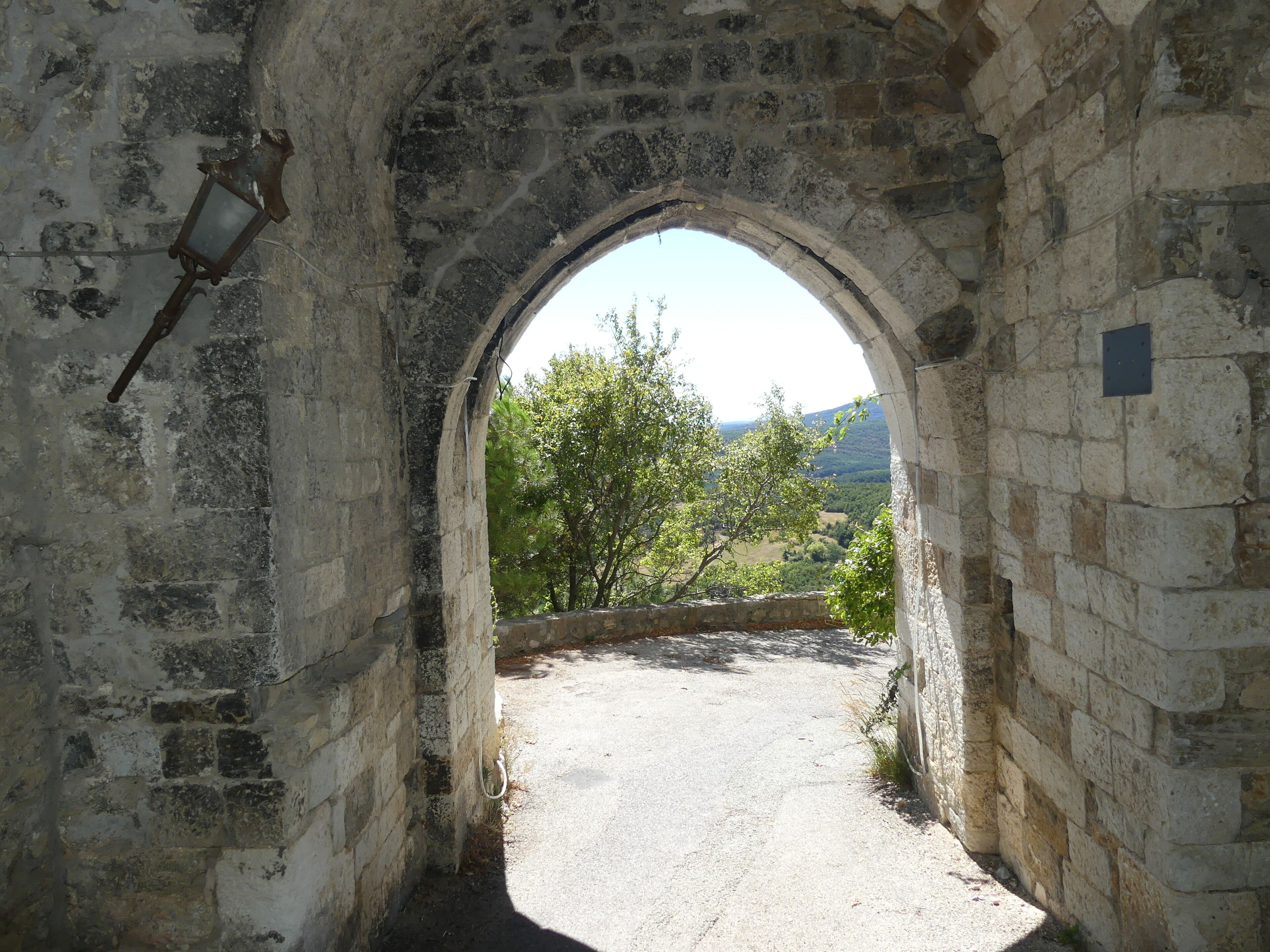 An arched stone doorway leading to a pathway with a view of a tree-lined landscape.