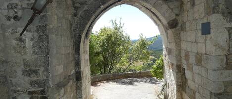 An arched stone doorway leading to a pathway with a view of a tree-lined landscape.