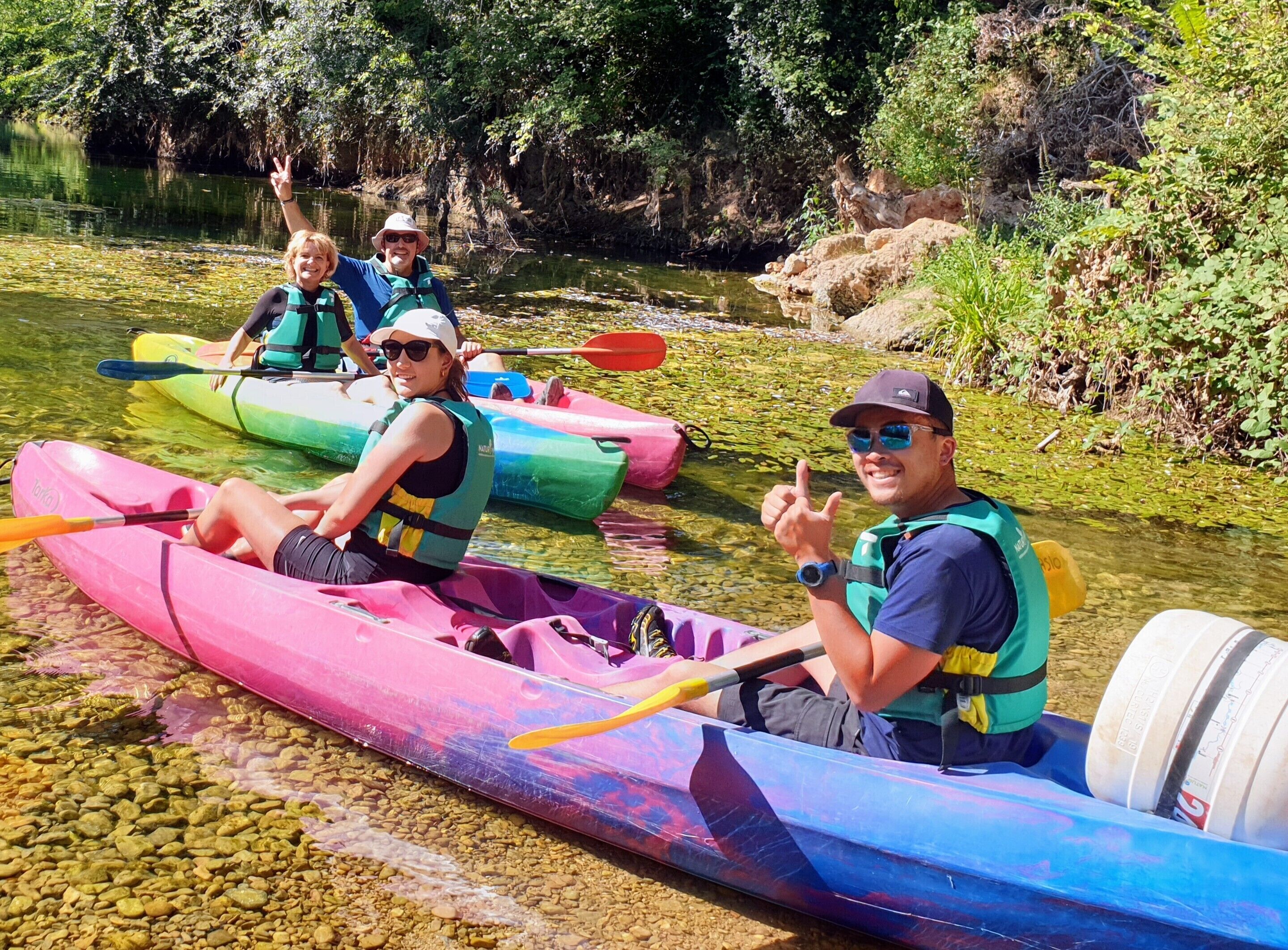 Un groupe de personnes pratiquant le kayak sur une rivière paisible, entourée de verdure.