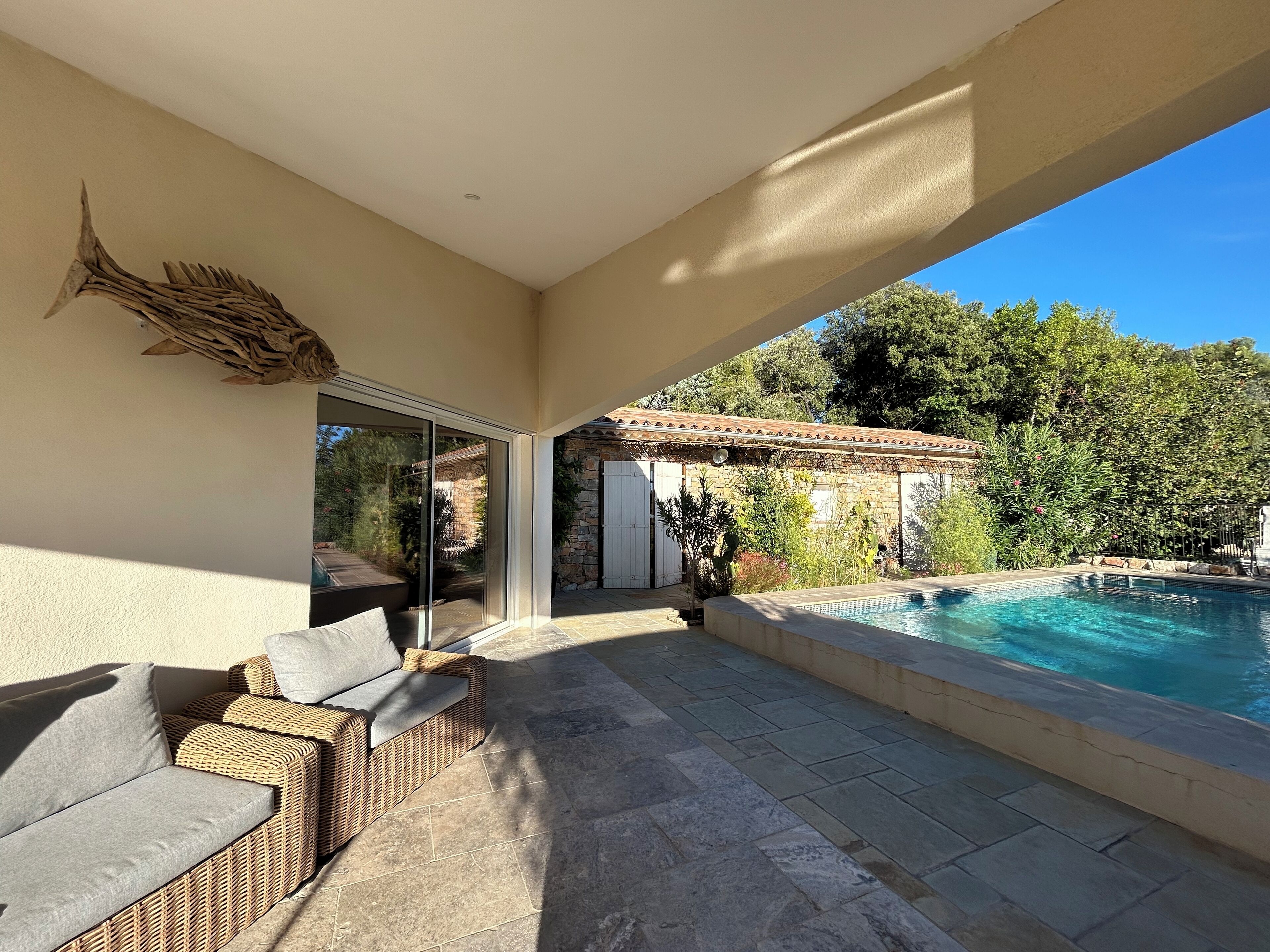 Um pátio externo com piscina, móveis de vime e uma parede de pedra.