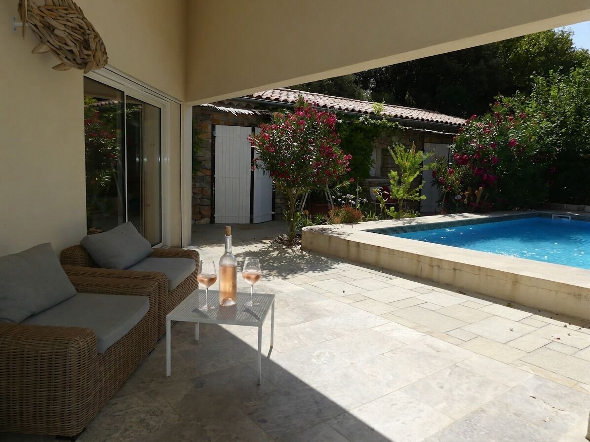 A patio with a pool, wicker furniture, and a glass table with a wine bottle.