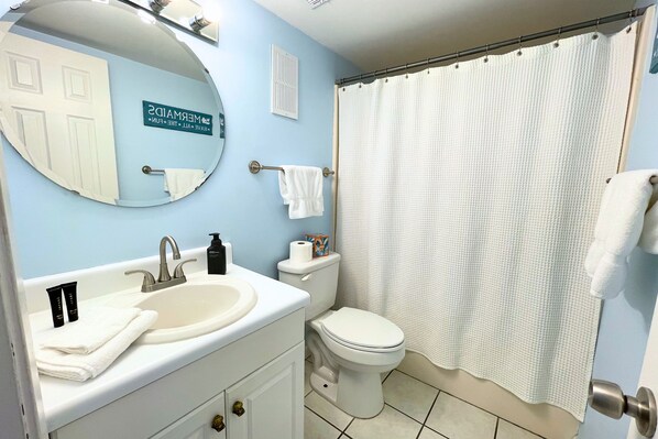 A bathroom with a sink, mirror, toilet, and shower curtain.