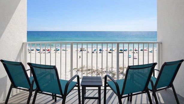 Balcón con vista a una playa, que incluye una mesa y cuatro sillas.